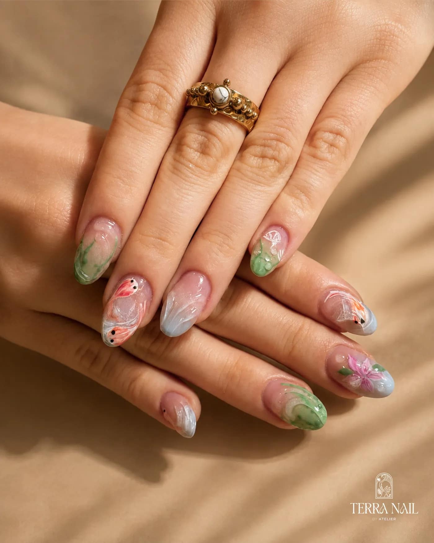 A hand wearing gold rings, with translucent nails hand-painted with botanical designs in green and pink