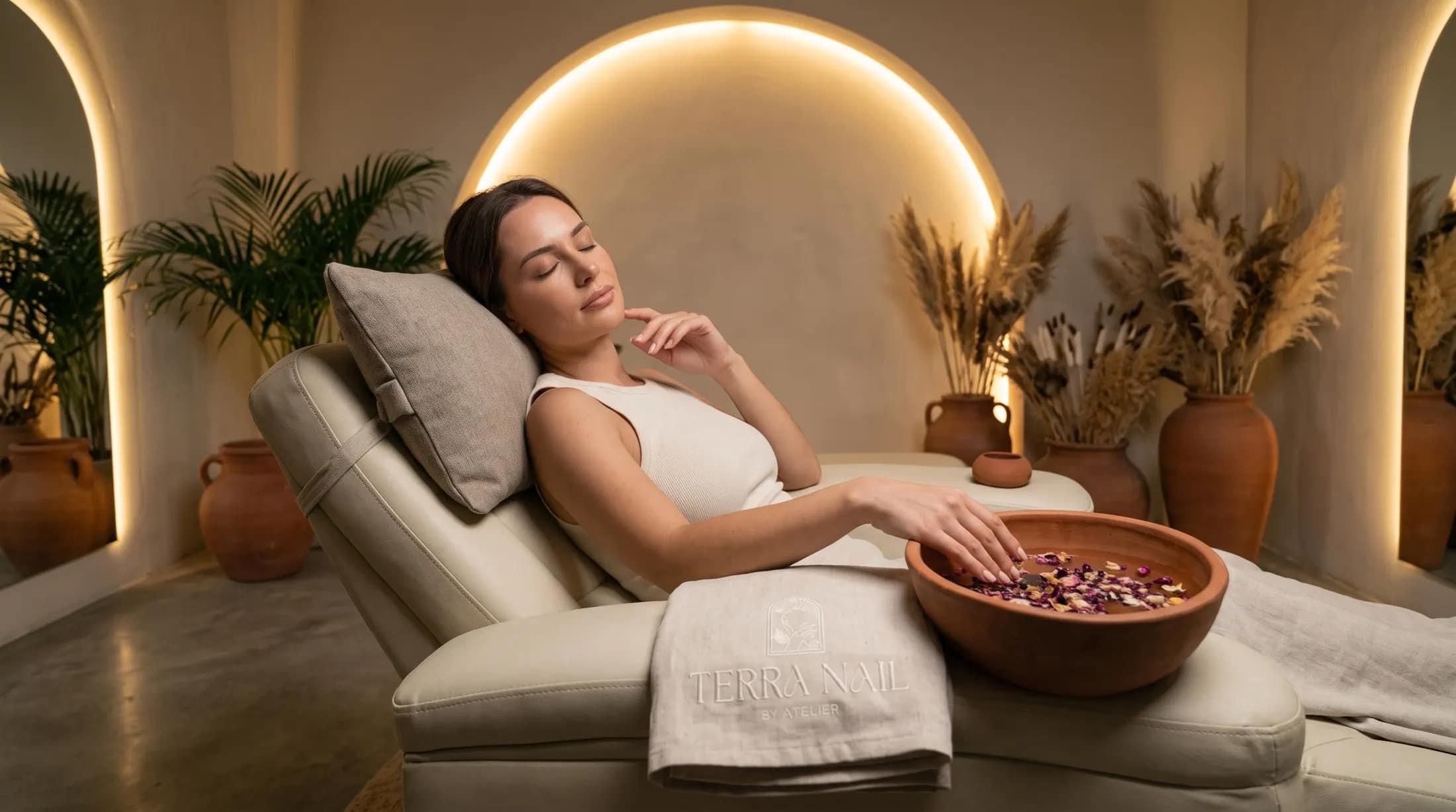 A client relaxing with her hand in a flower-filled bowl at Terra Nail, beneath a softly lit arch
