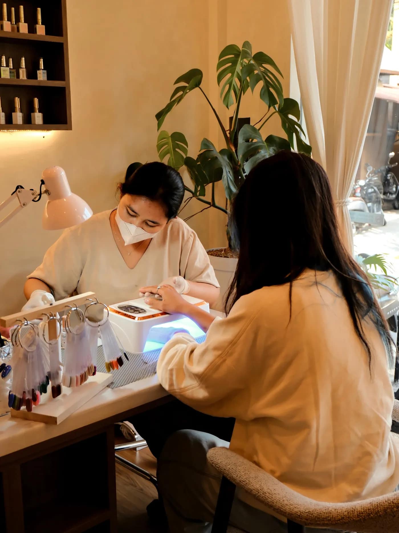 A Terra Nail technician working on a client's nails under a lamp at the studio bench